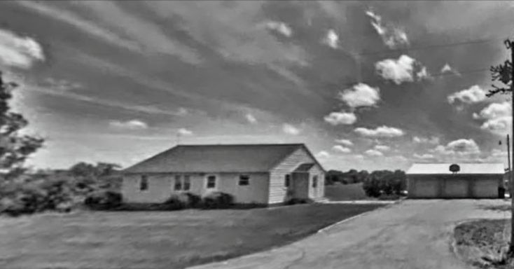 Single-story house with a garage, set against a cloudy sky and grassy landscape.