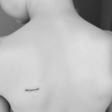 Close-up of a person's bare back with a small tattoo near the shoulder blade.