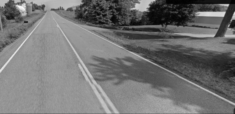 Long rural road lined with trees, featuring a double white lane marking.